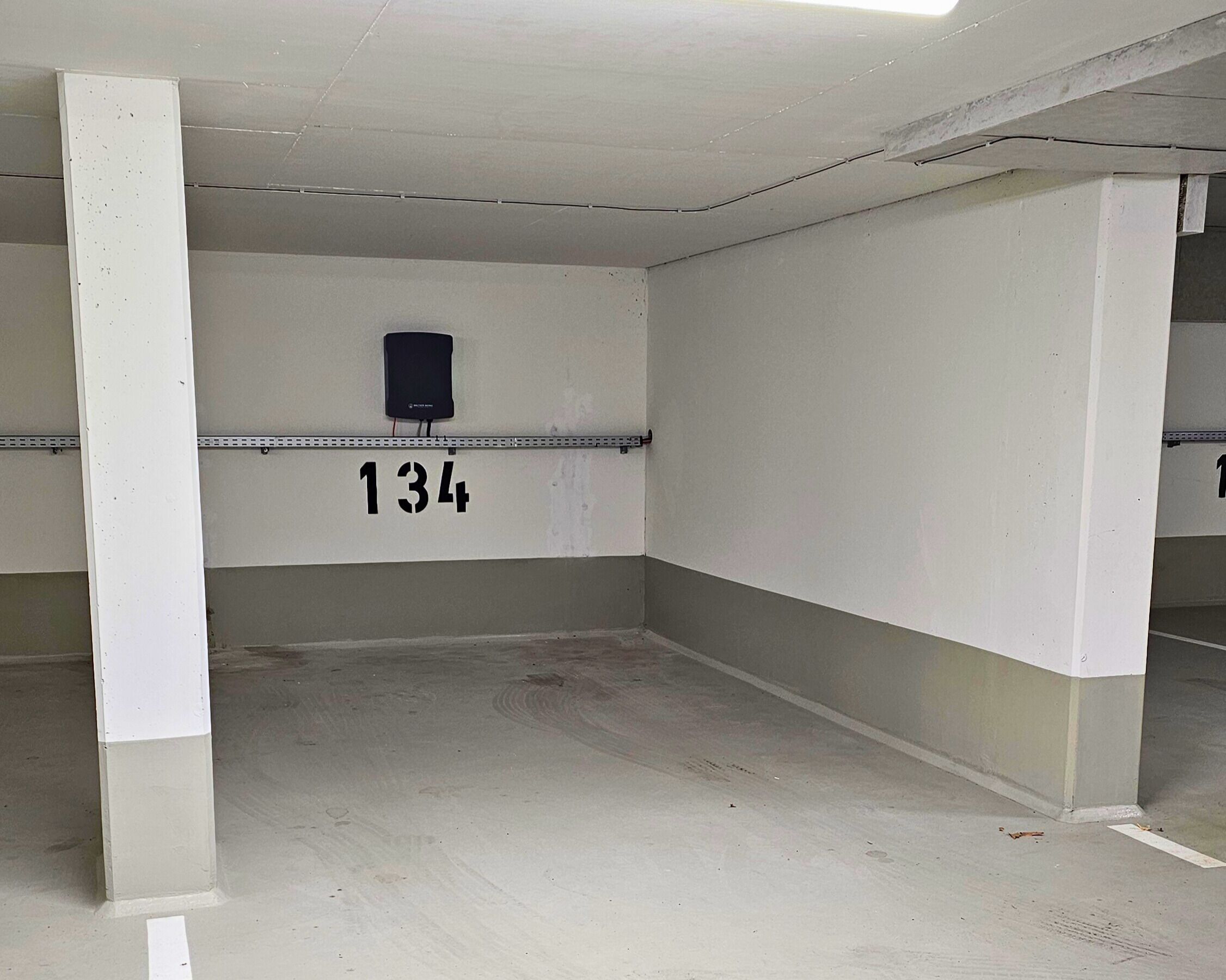 A parking garage with white walls, numbered parking spaces, and a black speaker mounted on the wall.