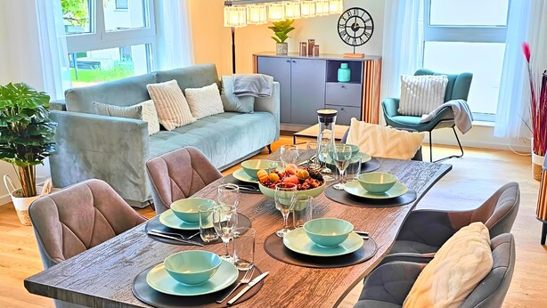 A dining area with a wooden table set for four, surrounded by grey upholstered chairs. - RelaxRefugium / 6 pers. / Garage / 2xWorkspace (Königs Wusterhausen)