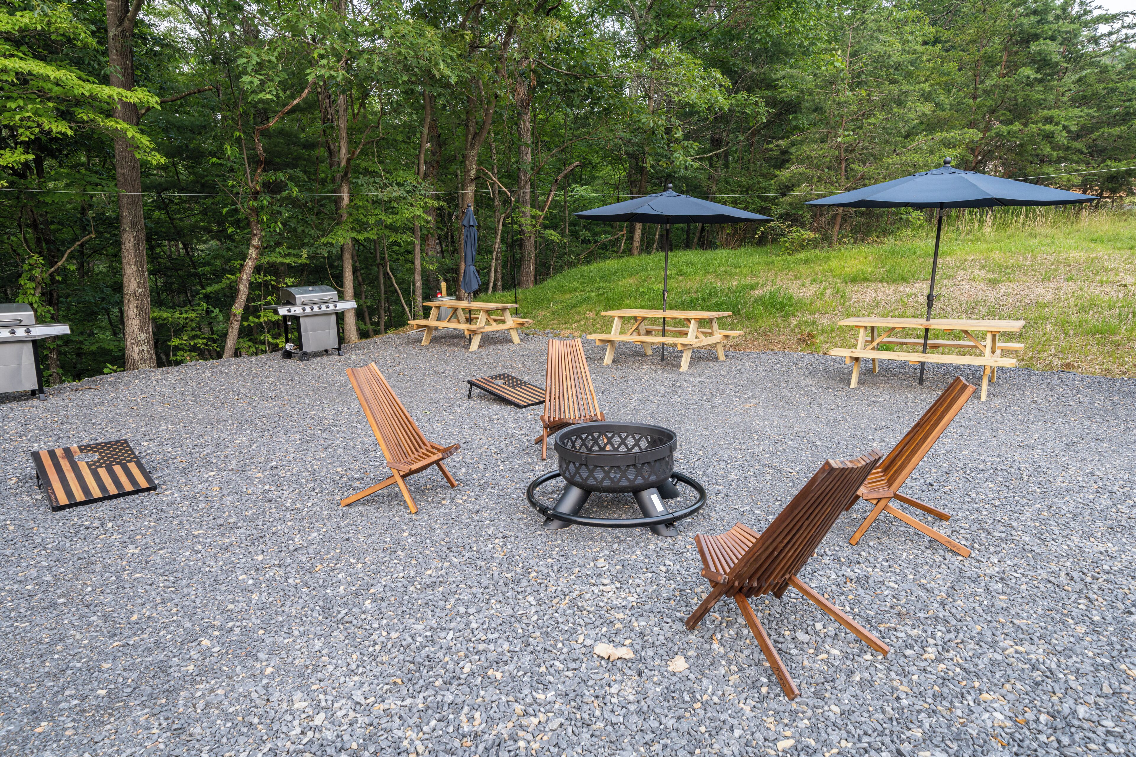 A gravel patio with picnic tables, lounge chairs, and a fire pit.