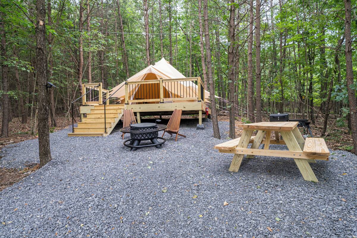 Ein bewaldeter Campingplatz mit einer Holzhütte, einer Feuerstelle und Picknicktischen.