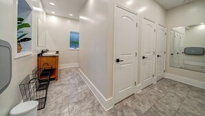 A modern bathroom with white walls, a large mirror, a sink, and a toilet. There are three white doors and a wooden cabinet with a plant. - Firefly Ridge (Great Cacapon)