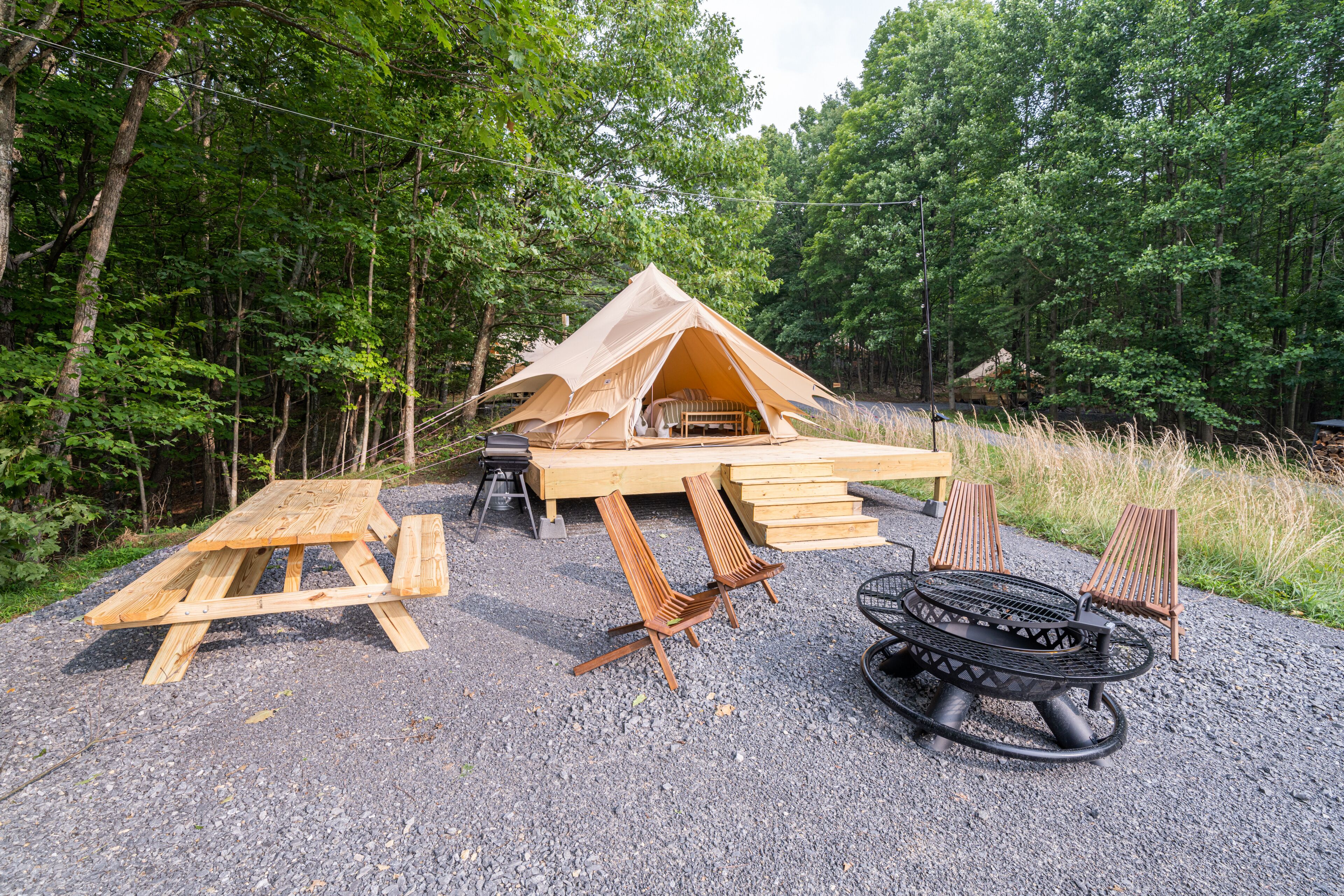 A tent with a picnic table and chairs, surrounded by trees.