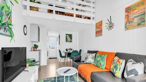 A modern living room with a grey sofa, a TV, a small white table, and a dining area with chairs. - On the Water 6  A One-of-a-Kind Stay | Free Parking | By My Getaways (Brighton)