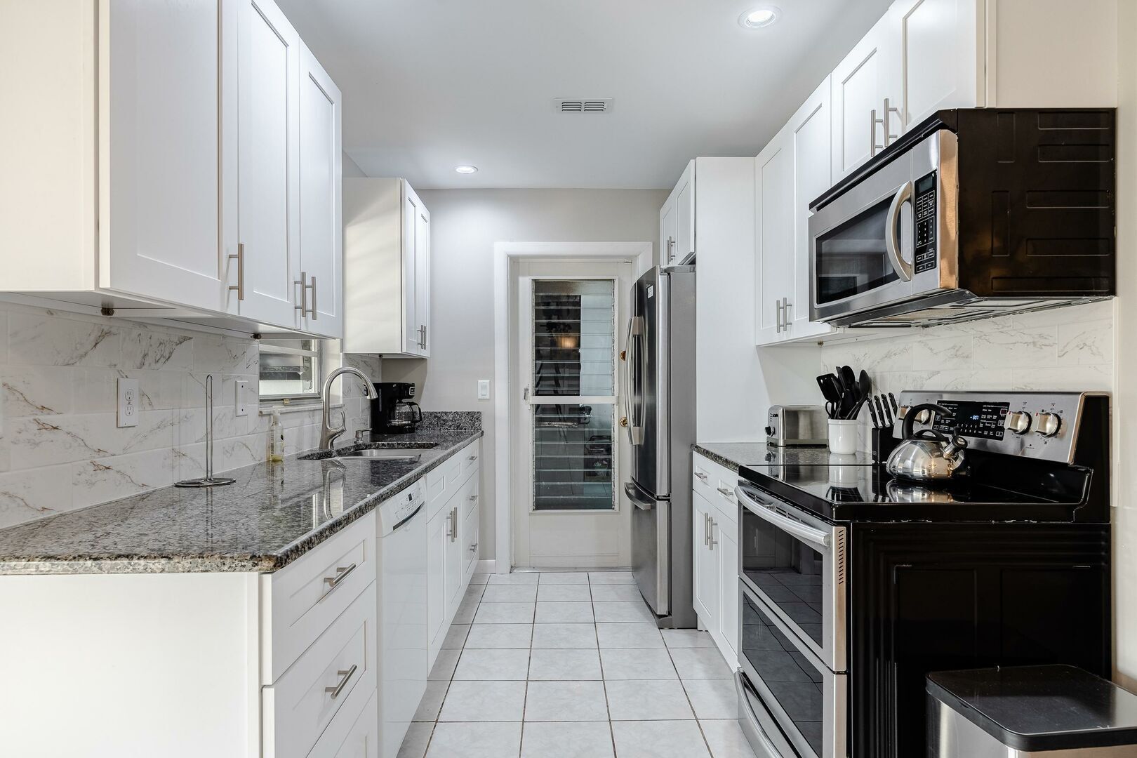 A modern kitchen with white cabinets, a granite countertop, stainless steel appliances, and a tiled backsplash.