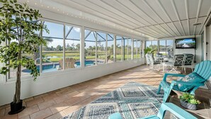 Une terrasse couverte avec vue sur une piscine, du mobilier d’extérieur et un téléviseur.