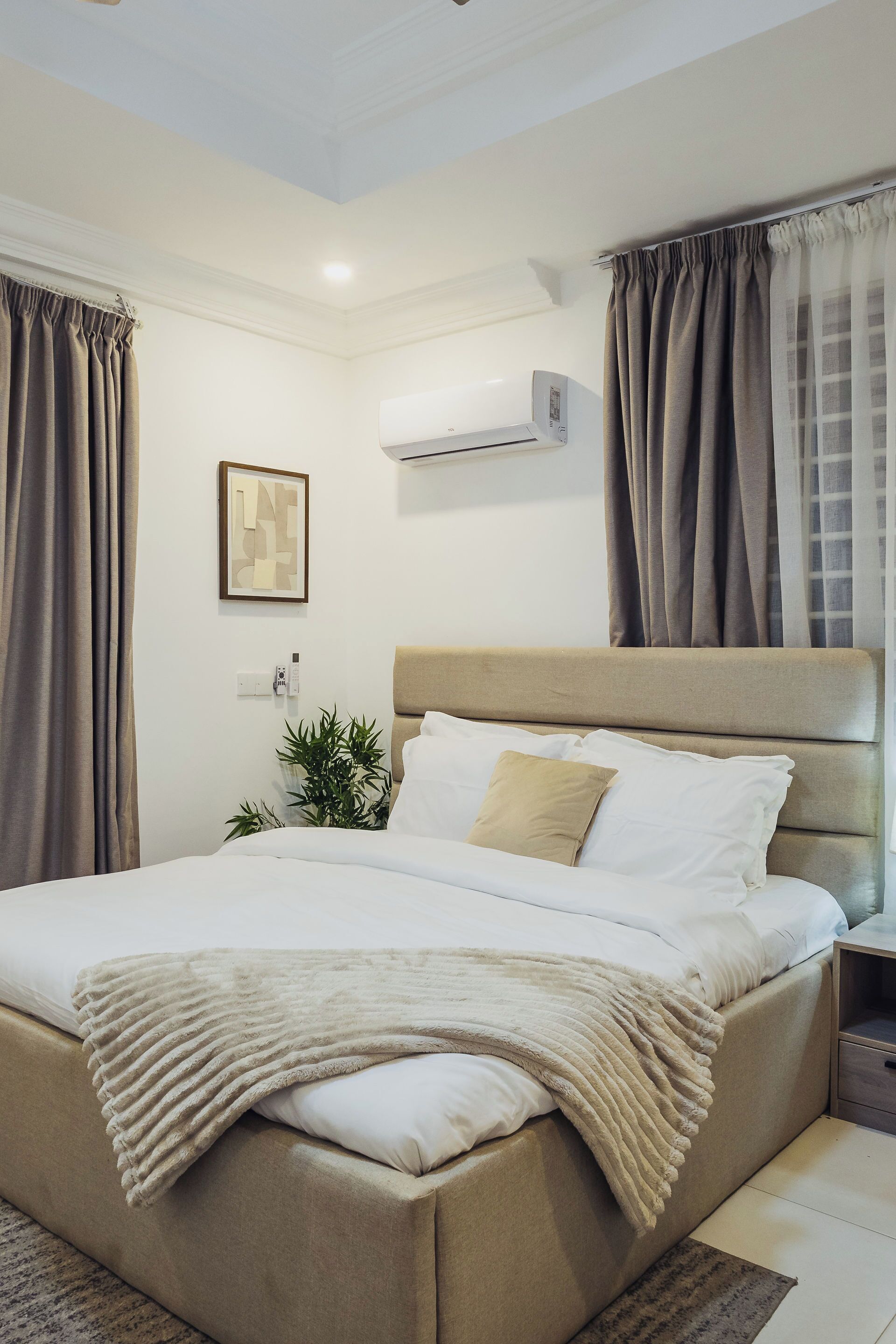 Ein modernes Hotelzimmer mit einem großen Bett, beigen Vorhängen, einer Klimaanlage und einem gerahmten Bild an der Wand.