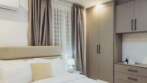 Una habitación de hotel con cama, mesita de noche, lámpara, ventana con cortinas y armario.