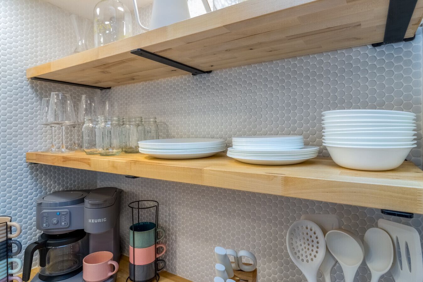 Une cuisine avec des étagères en bois où sont rangés de la verrerie, des assiettes et une machine à café.