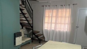 Een kamer met een tafel, een stoel, een trap, een raam met gordijnen en een deur.