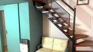 Een kamer met een blauwgroene bank, een trap met metalen leuning en een witte muur met een fotolijst.