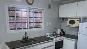 Een keuken met witte kasten, een gasfornuis, een spoelbak, een magnetron en een klok aan de muur.