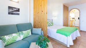 Une chambre moderne avec un canapé vert, un lit recouvert d’une couverture verte, une cloison en bois et un tableau représentant un pont, accroché au mur.