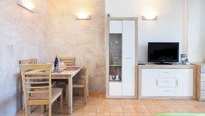 Un espace de vie compact comprenant un coin repas, un téléviseur et un meuble contenant de la vaisselle.