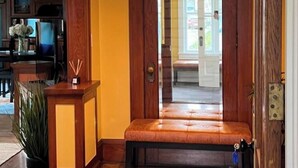 Eine Holztür mit einer Bank davor, ein Eingangsbereich mit Teppich und ein Blick in den Küchenbereich.