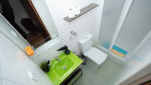 Un baño con un lavamanos verde, un inodoro blanco y una zona de ducha.