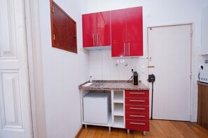 Una cocina compacta con armarios blancos, una encimera roja y una puerta blanca.
