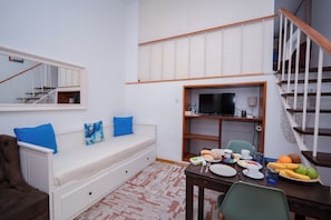 A room with a bed, a dining table with plates and cups, a TV, and a staircase. - Room-palma 1 Bedroom Apartment Lisbon (Lisbon)