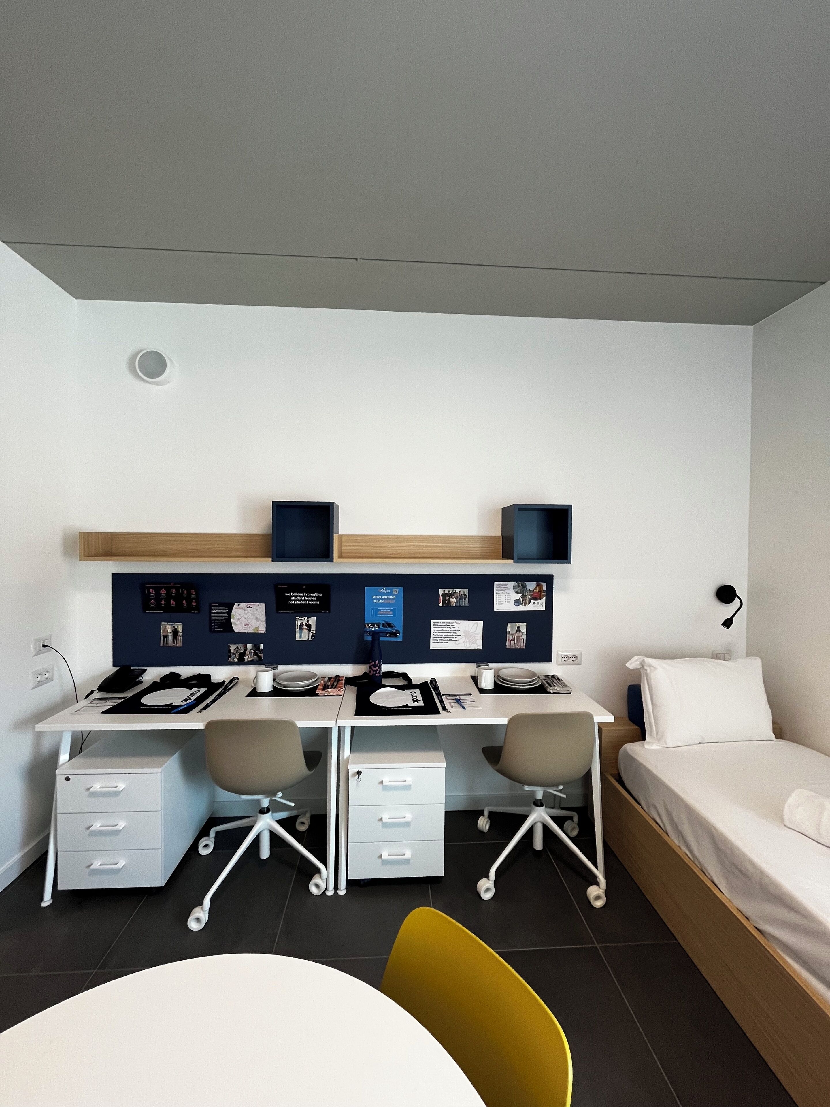 Una habitación de hotel moderna con escritorio, dos sillas, una cama y una pequeña mesa de comedor.