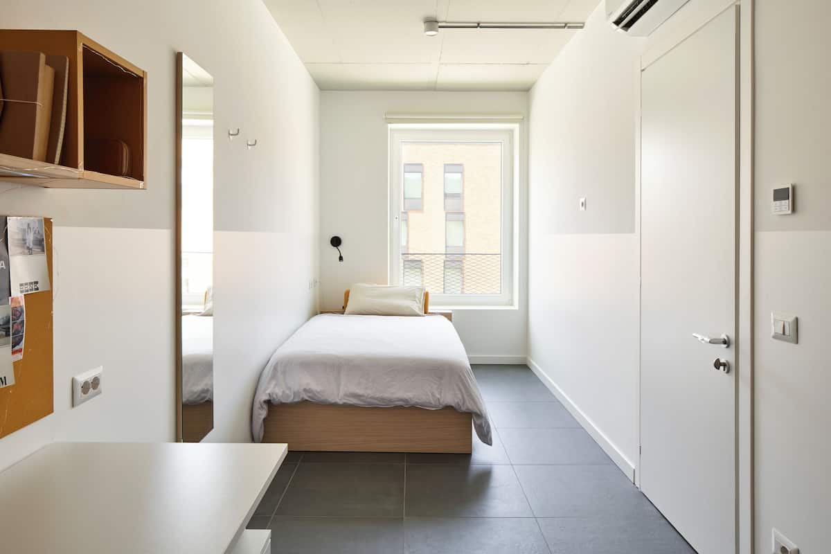 A modern bedroom with a bed, a desk, and a window.