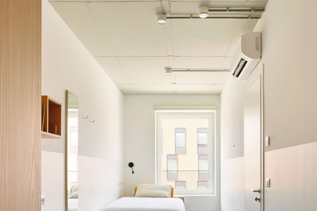 A bedroom with a bed, desk, chair, wardrobe, and a window.