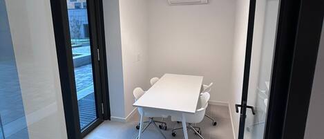 Una sala de reuniones moderna con una mesa y sillas blancas, una lámpara en el techo y un equipo de aire acondicionado.