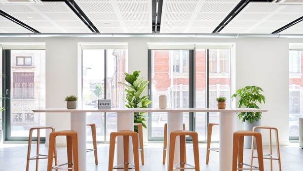 A modern office space with a long table and wooden stools, large windows with city views, and potted plants. - aparto Milan Durando (Milan)