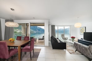 A modern living room with a dining area, a sofa, a TV, and a view of the mountains.