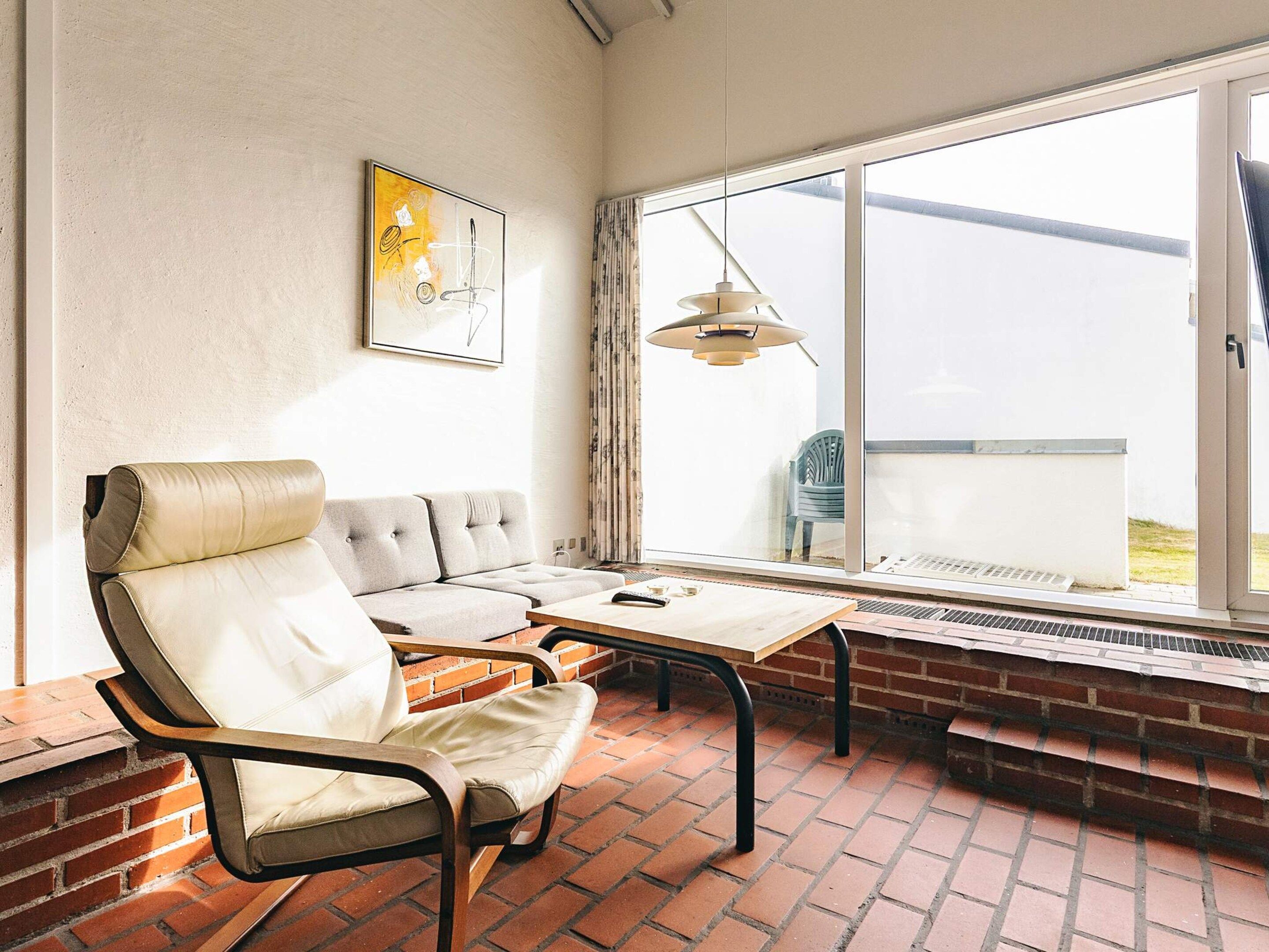 A room with a sofa, a table, a hanging light fixture, and a window with a view.
