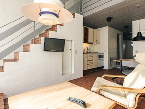 Une cuisine moderne équipée d’un téléviseur à écran plat, d’un coin repas avec une table et des chaises en bois, et d’un escalier avec un mur en briques.