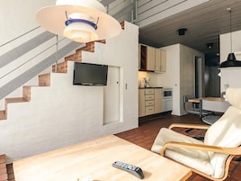 Una cocina moderna con una televisión de pantalla plana, un comedor con mesa y sillas de madera, y una escalera junto a una pared de ladrillo.