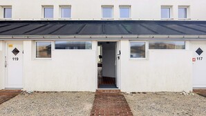 A two-story building with numbered doors, a flat roof, and a gravel driveway. - 6 Person Holiday Home in Brovst (Brovst)