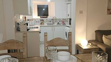 Cocina compacta con televisor, lavadora y comedor con mesa para dos.