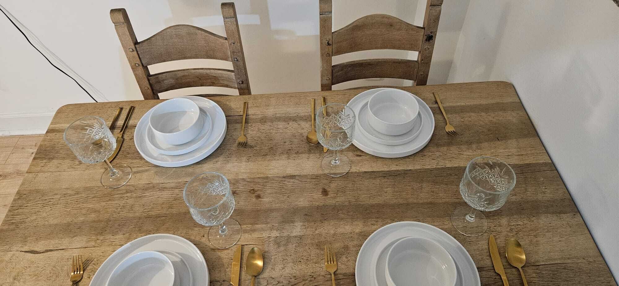 A wooden dining table set with white plates, bowls, and cutlery.