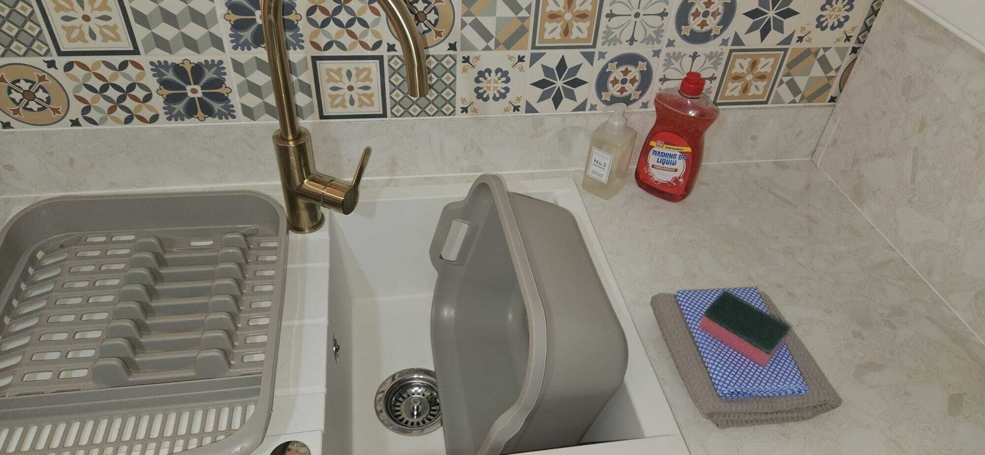 Une salle de bain avec une baignoire, une douche, un lavabo avec un robinet, un flacon de savon liquide et une éponge sur le sol.