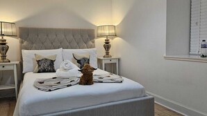 Uma cama bem arrumada com cabeceira estofada, duas luminárias laterais e uma pequena estatueta sobre a cama.