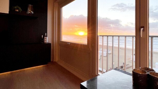 Un soggiorno moderno con una grande finestra vista spiaggia al tramonto.