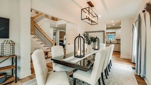 A modern dining area with a glass-top table, white upholstered chairs, and a wooden floor.