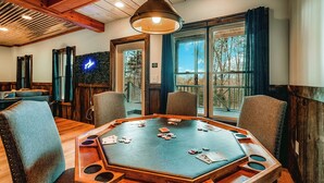 A poker table in a room with wooden beams, large windows, and a view of trees.
