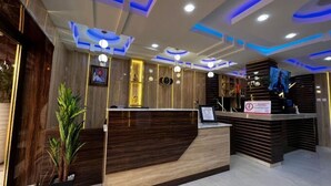 A modern reception area with a wooden reception desk, a potted plant, and a TV screen. - LINKS HOTEL  (Owerri)