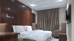 A hotel room with a bed, two chairs, a desk, and a TV on the wall. - LINKS HOTEL  (Owerri)