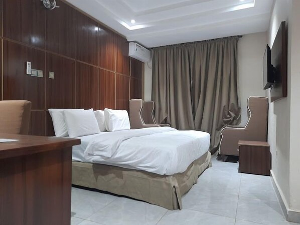 A hotel room with a bed, two chairs, a desk, and a TV on the wall.