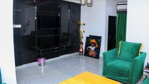 A modern living room with a flat-screen TV, a green armchair, a vase with flowers, and a framed picture on the wall. - LINKS HOTEL  (Owerri)