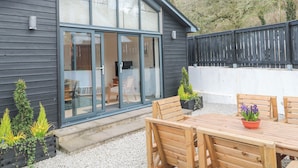 A modern house with a large glass door leading to a patio area with wooden furniture and potted plants.