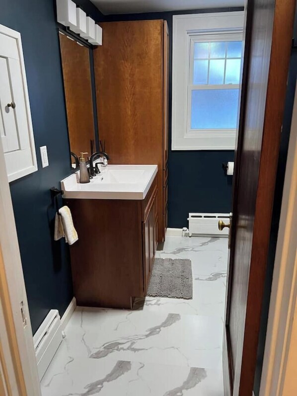 A bathroom with a wooden vanity, white sink, and a window providing natural light. - CRAFTSMAN’sUPSTAIRS! 3 bd rm w/impressive attic! (Willmar)