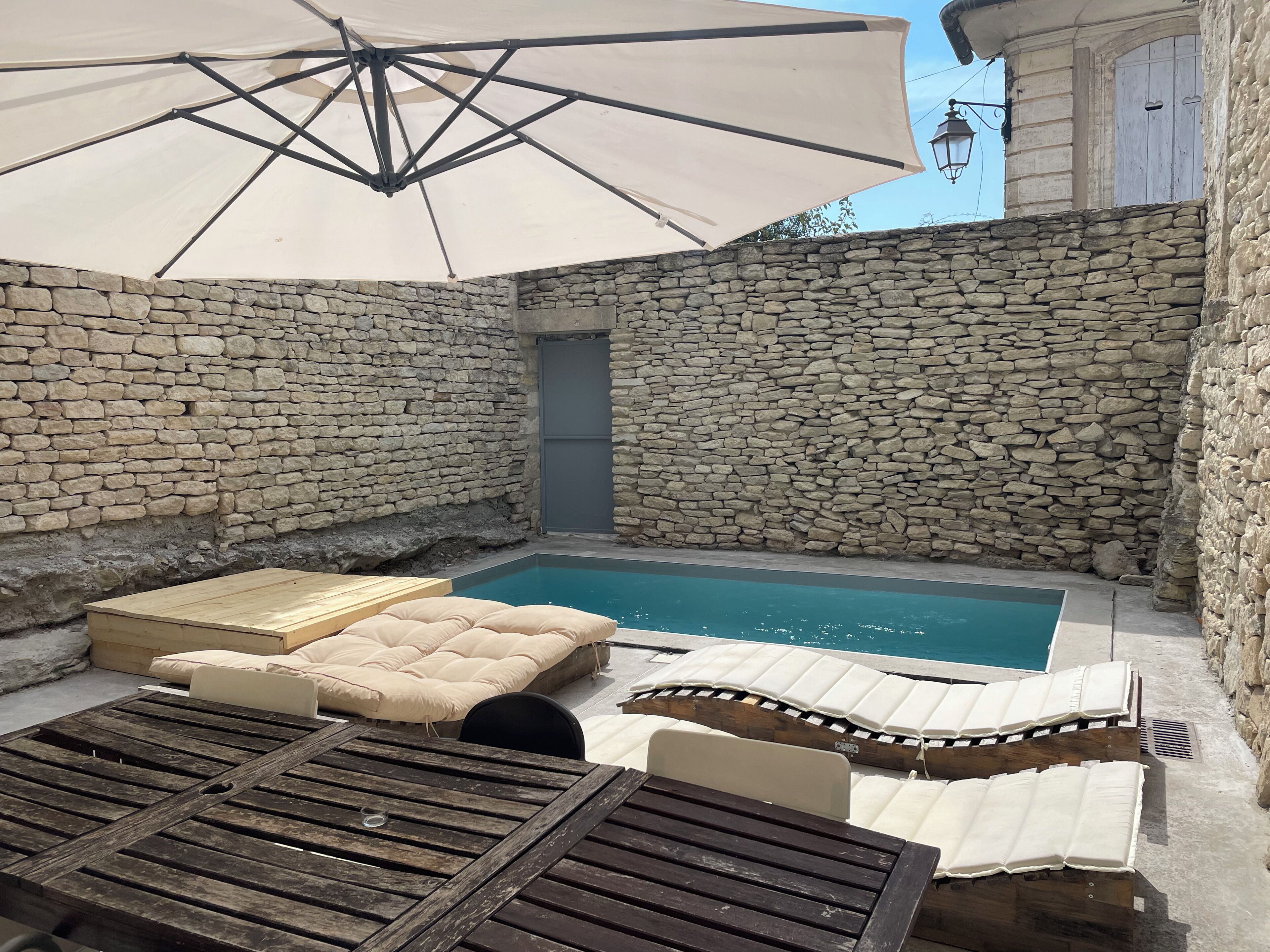 Et udendørs område med stenvægge, en pool, liggestole og en parasol.
