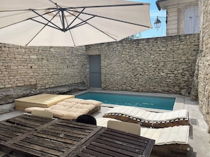 A stone-walled outdoor area with a pool, lounge chairs, and an umbrella.