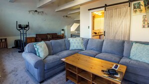 Ein modernes Wohnzimmer mit einer Eckcouch, einem Holztisch und einem Deckenventilator.