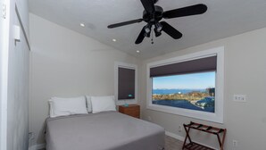 Ein Schlafzimmer mit Bett, Deckenventilator, Fenster mit Blick auf die Stadt und Nachttisch.