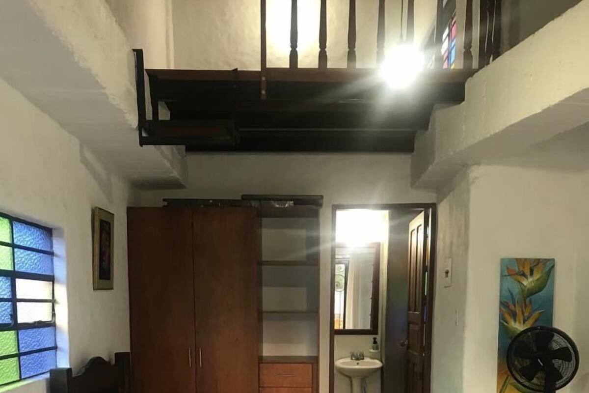 A room with two beds, a wooden wardrobe, a small bathroom, and a balcony with a railing.
