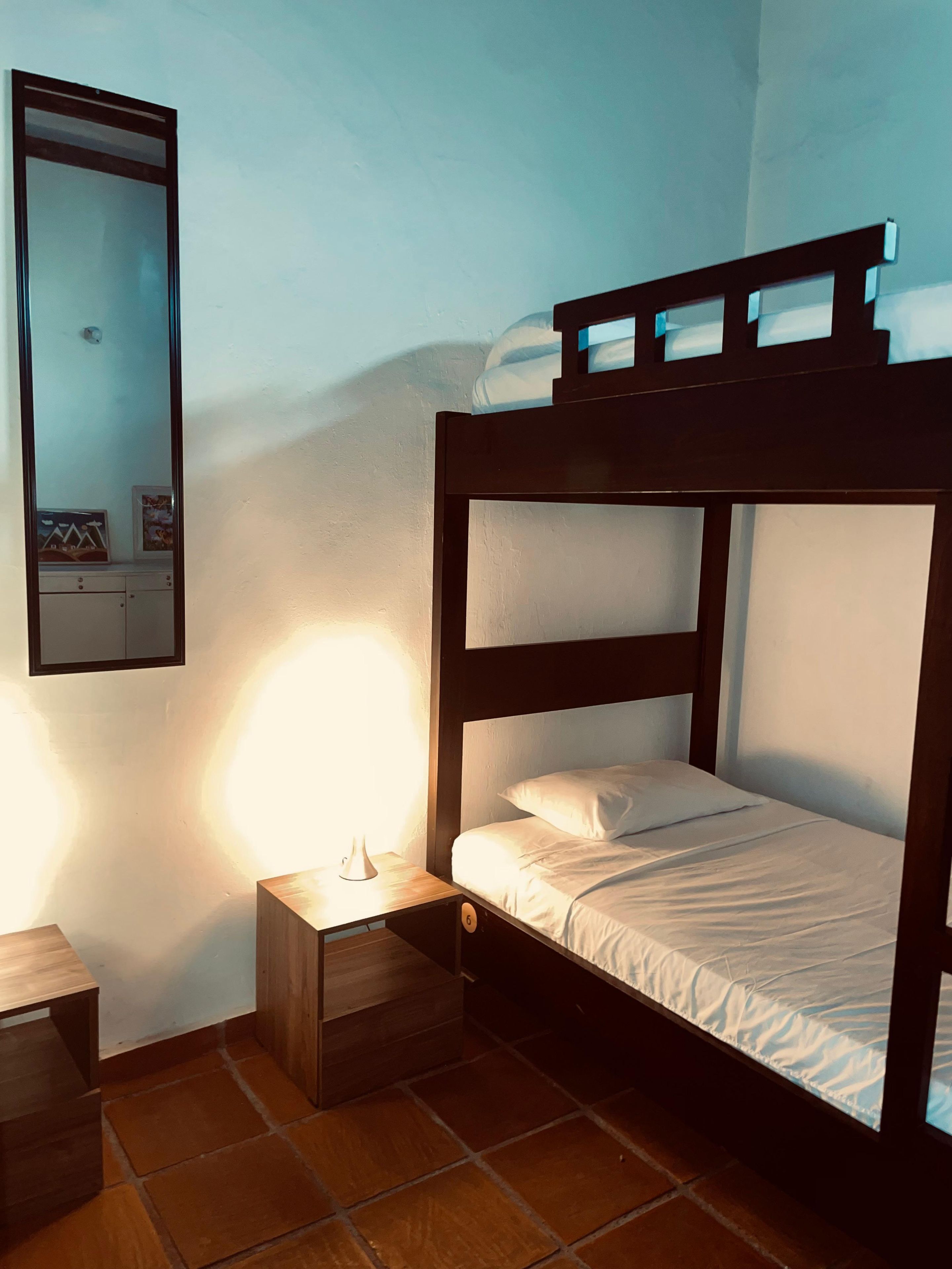 A bunk bed with a wooden frame, a bedside table with a lamp, and a wall-mounted mirror.